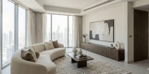 Modern minimalist living room with curved beige sofa, floor-to-ceiling windows, city skyline views, and neutral color palette